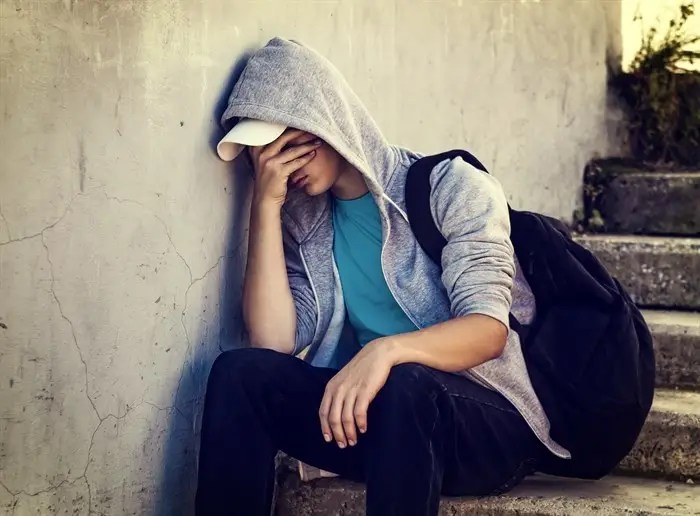 Non-police mental health crisis response team coming to Kelowna | iNFOnews.ca A young person wearing a hoodie and a backpack sitting on stairs with a hand on their face.