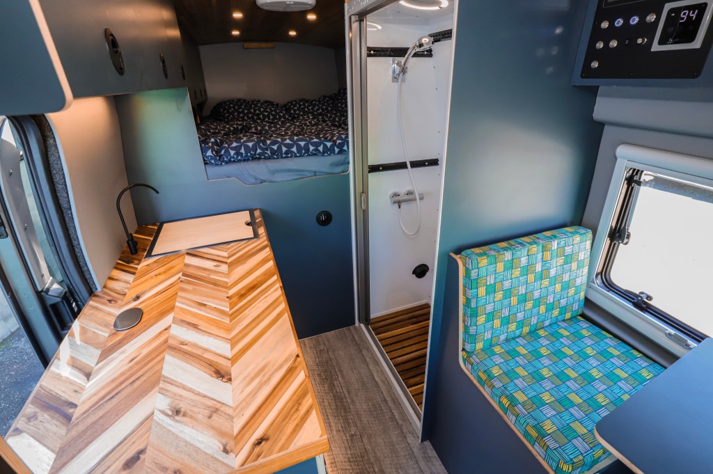 The interior of a custom campervan with a double bed, kitchen side and table. 