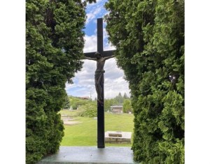 A statue of Jesus in a cemetery with shrubs on either side.