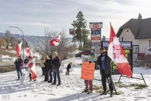 Freedom Convoy supporters waving flags and holding signs on a snowy lawn.