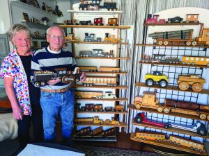 An elderly woman and man stand in front of a shelf full of wooden toys.