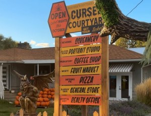 A decorative orange wooden sign displays a list of shops at a Halloween display.