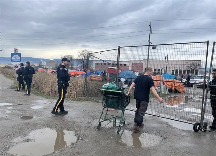 A man waiting to get let through a temporary fence into a homeless camp.