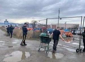 A man waiting to get let through a temporary fence into a homeless camp.