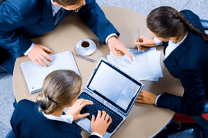 People sitting around a desk, working on a laptop and signing papers.