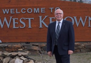 A man in a suit stands in front of a Welcome to West Kelowna sign.