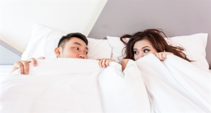A couple under white blankets in a bed.