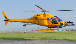 A yellow helicopter about to take off with a LiDAR scanner on the front.