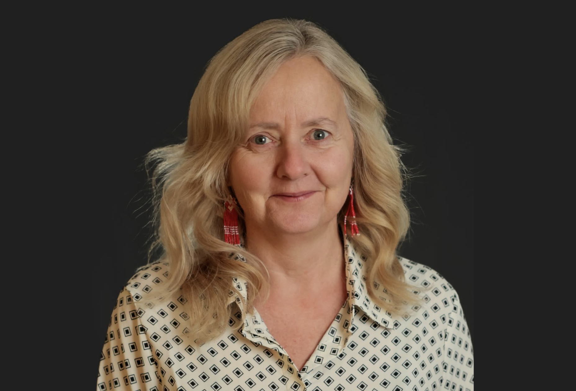 Sylvia Weir poses for a photo in a white shirt on a dark background.