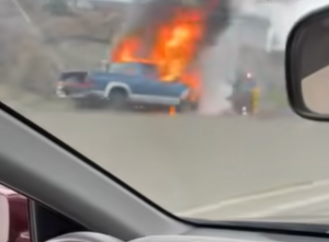 A pick up truck on fire on a road.
