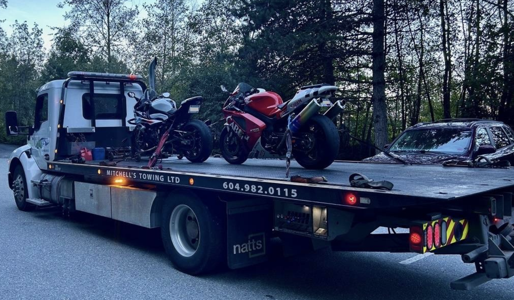 Two motorcycles on the back of a tow-truck.