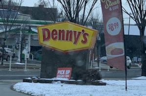 A Denny's restaurant sign on a snowy lawn.