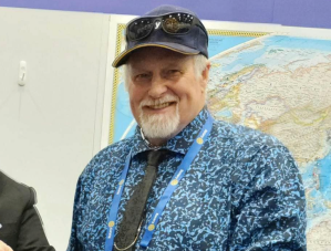 Wearing a shirt and tie and a baseball cap a man smiles as he had his photo taken