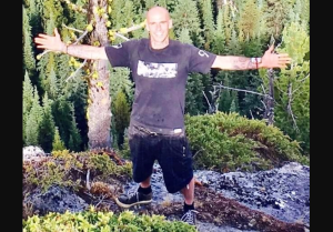 A man stands in a wooded area with his arms outstretched.