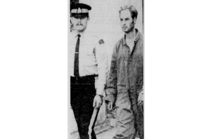 A black and white photo of an police officer walking handcuffed with a prisoner.