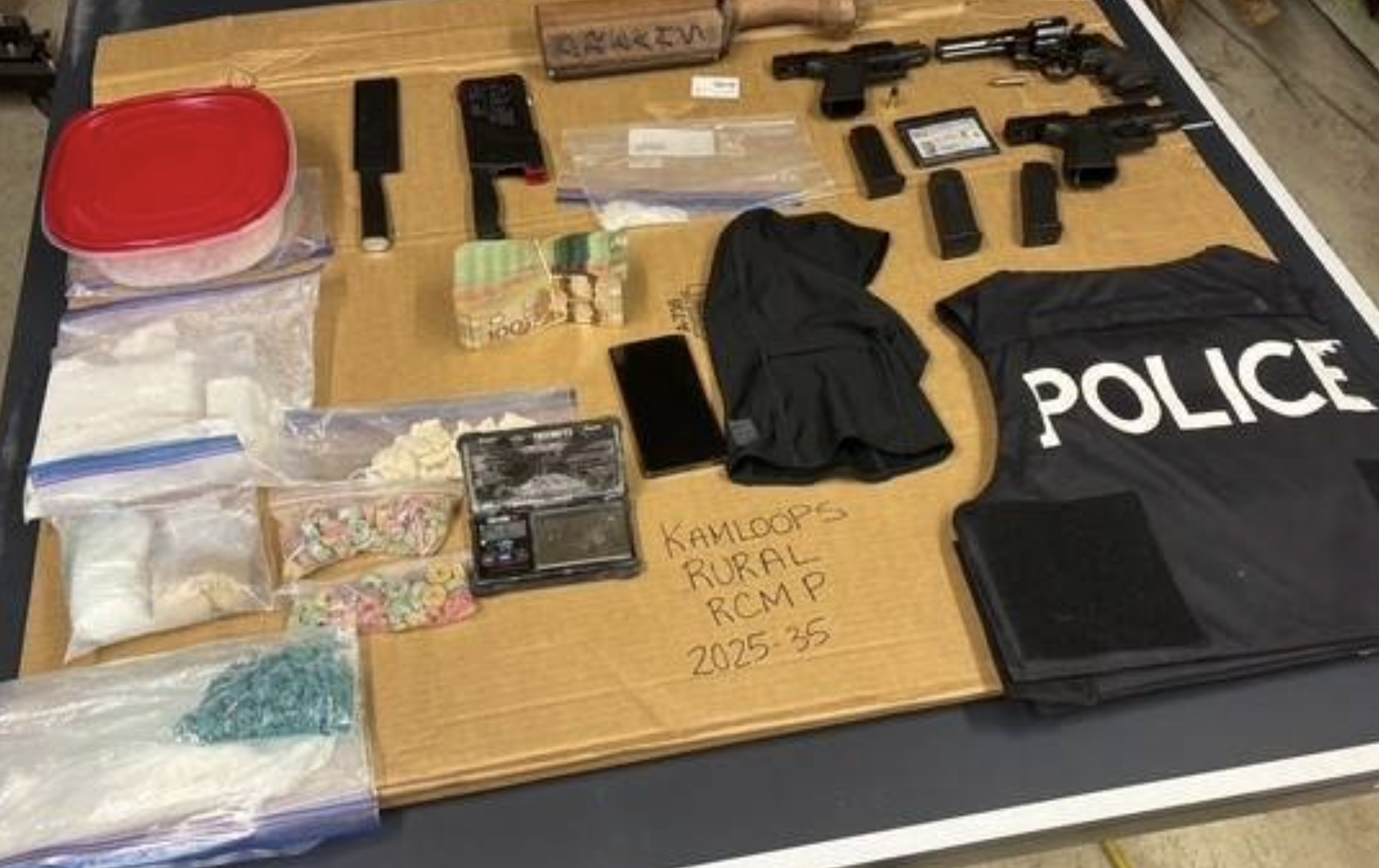 Kamloops RCMP find cash, drugs, guns in rented vehicle | iNFOnews.ca Drugs and guns laid out on a table with a police vest.