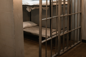 A bed seen through the bars of a prison cell.