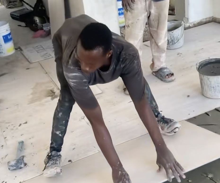 A guy precariously laying down a huge tile.
