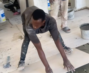 A guy precariously laying down a huge tile.