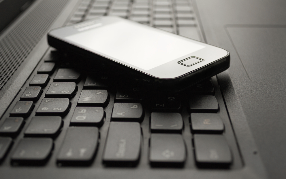 A cell phone rests on the keyboard of a laptop computer.