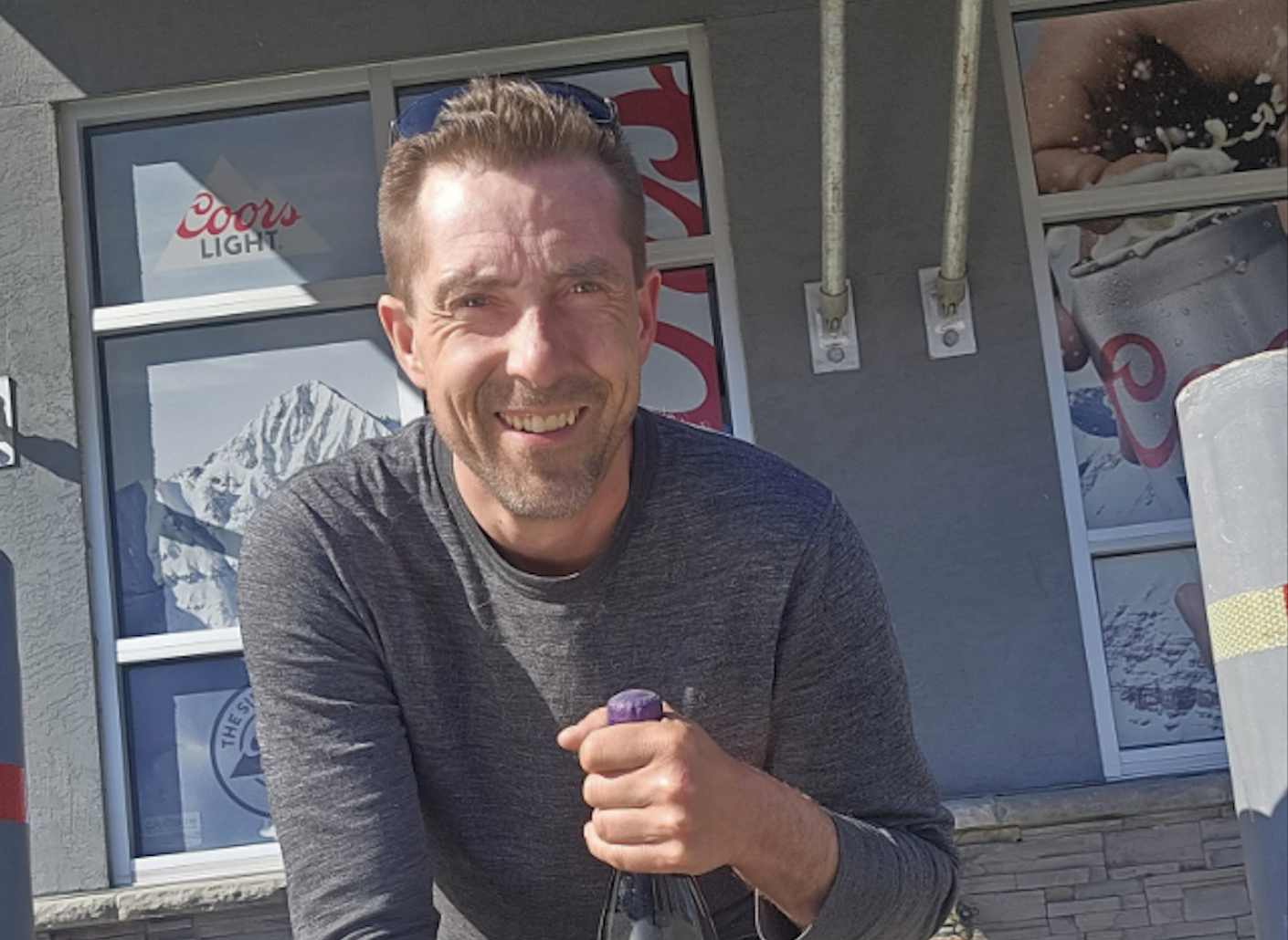 A man holds a bottle of wine outside a liquor store.