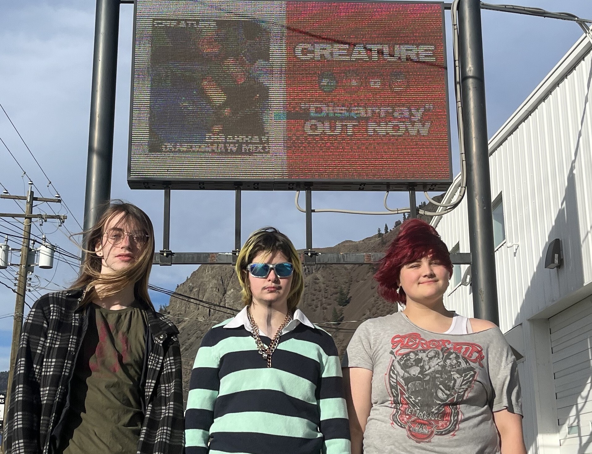iN VIDEO: Community support means growing success for young Kamloops rockers | iNFOnews.ca Three teenagers stand below a digital billboard.