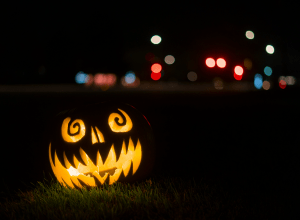 A lit Jack-o-lantern at night with blue and red lights in the background.