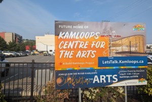 A billboard advertises an arts venue with a parking lot in the background