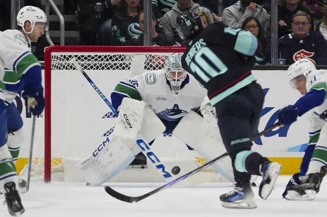 A hockey player for the Seattle Kraken taking a shot at the Vancouver Canuncks goaltender.