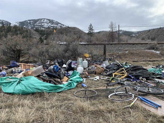 A pile of trash including tarps and bike parts lay in a grassy field.