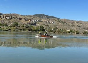 An aluminum boat carries two people on a river.
