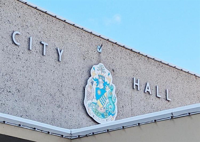 The words city hall with the Penticton coat of arms on the side of a building.