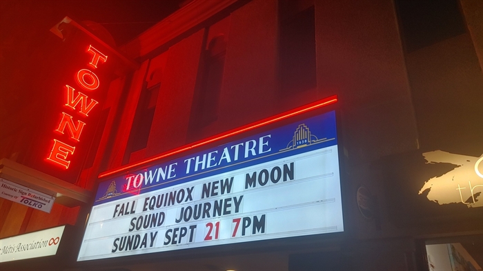 A marquee reading the word Towne glows orange above a lit up sign showing movie screenings.