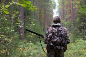A man dressed in camo clothing holding a rifle in the forest.