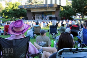People on lawn chairs watch a band playing on a stage.