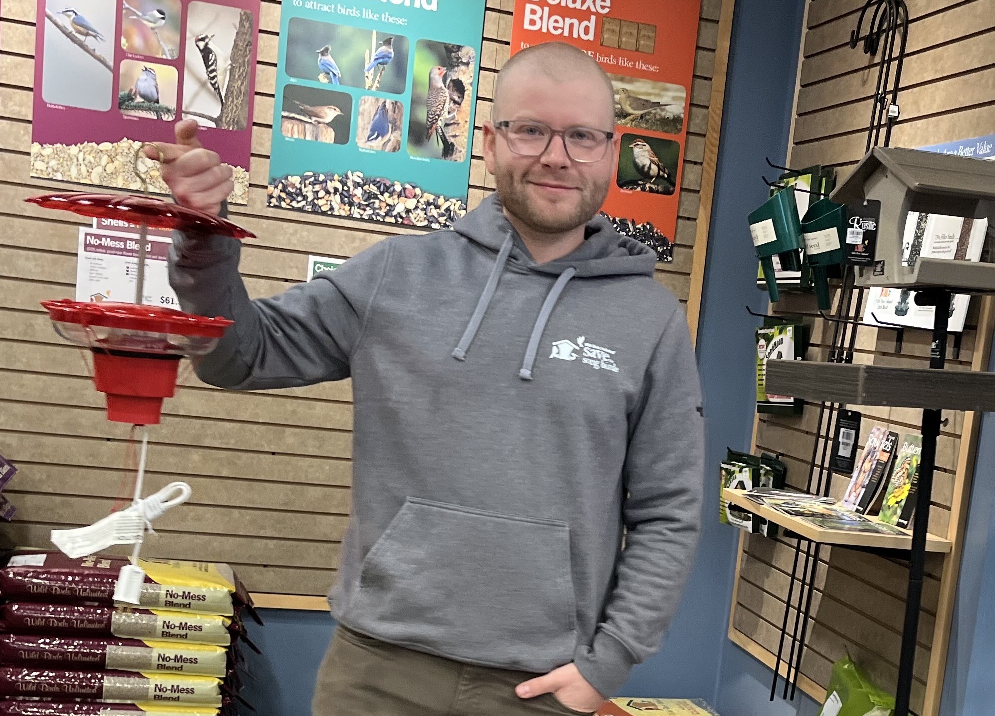 Hummingbirds in Okanagan, Kamloops in winter? Here's how you can help them survive | iNFOnews.ca A man holds a hummingbird feeder up with his left hand while his right hand is in his jeans pocket.