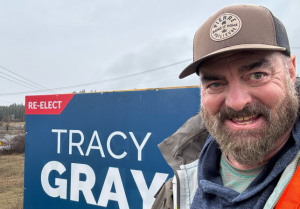 Man pictured in a selfie in front of an election sign.