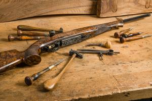 An old rifle lays on a workbench surrounded by tools.