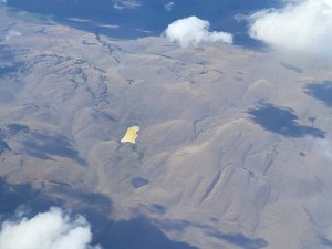 A yellow lake in far off mountains is pictured from the window of a commercial plane.